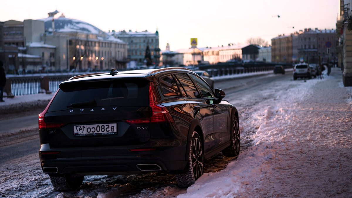 Black Volvo V60 parked on a snow-covered street in a winter city scene at sunset.