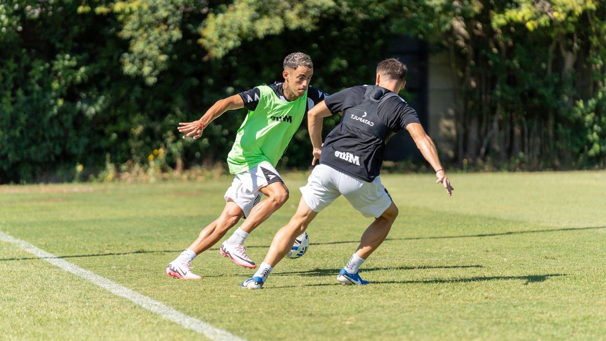 Two soccer players engage in strategic defense practice on a sunny day.