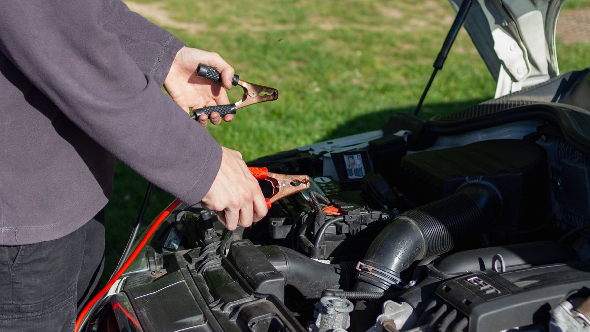 Close-up of mechanic using jumper cables to jump-start a car battery outdoors.