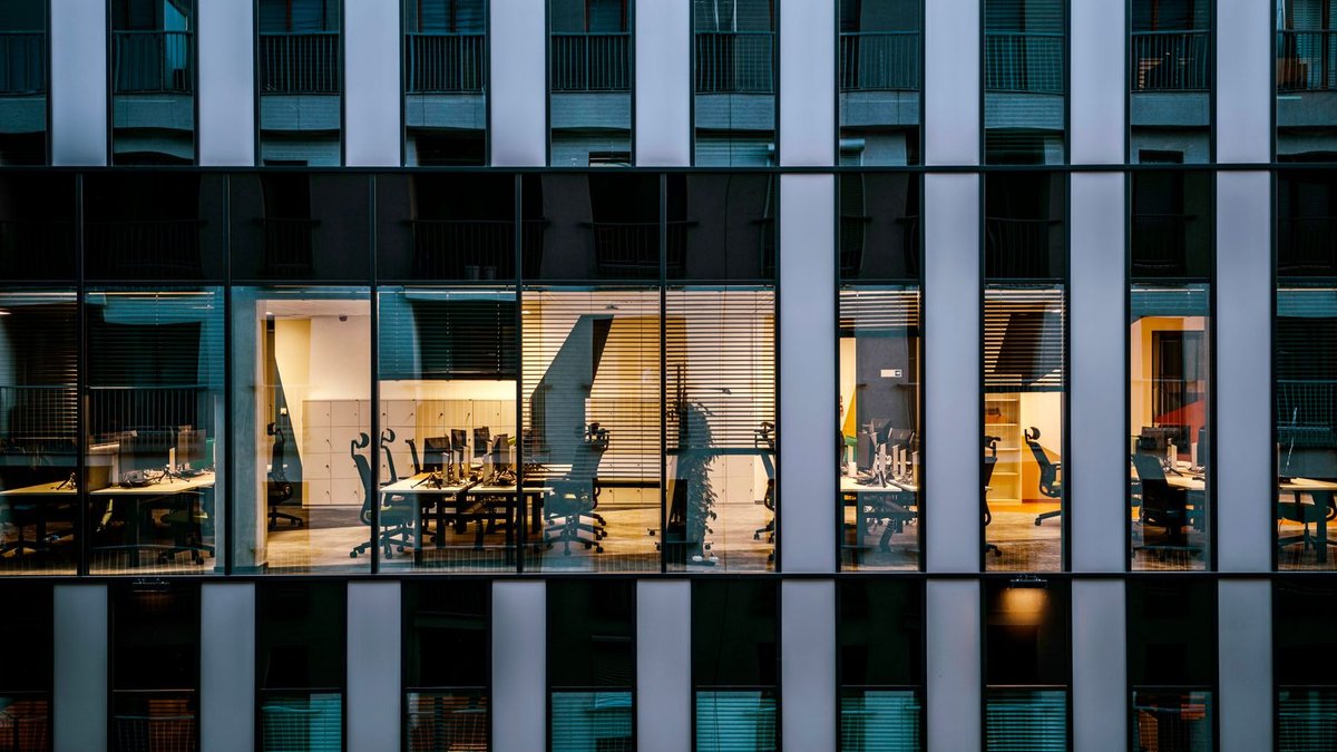 Illuminated office inside a modern glass building exterior, showcasing architecture and workspace design.
