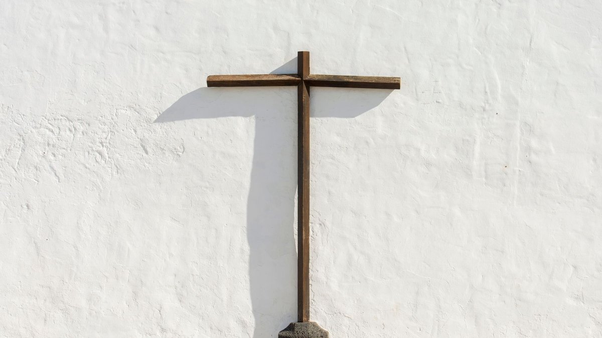 A simple wooden cross standing against a stark white wall, symbolizing faith and tranquility.