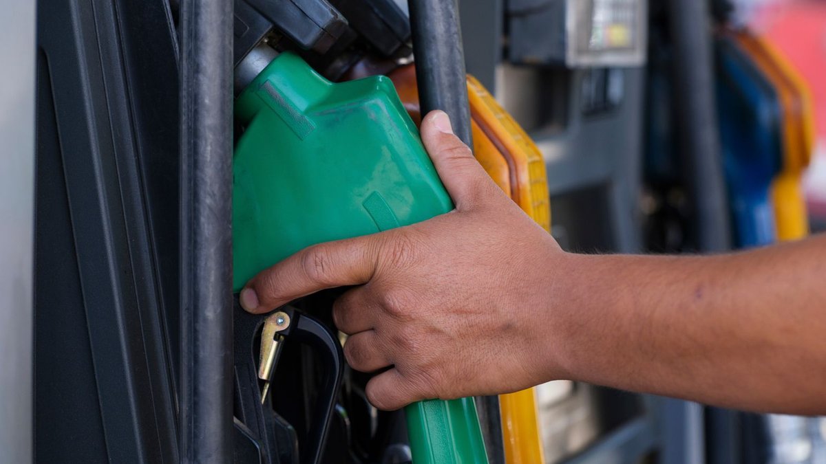 Close-up of a hand holding a green fuel nozzle at a gas pump station outdoors.