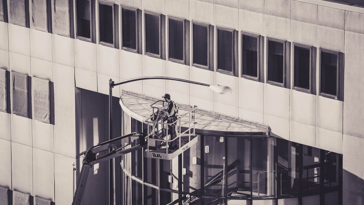 Trane Launches AI Platform for Building Maintenance A construction worker on a hydraulic lift conducts maintenance on a modern building facade.