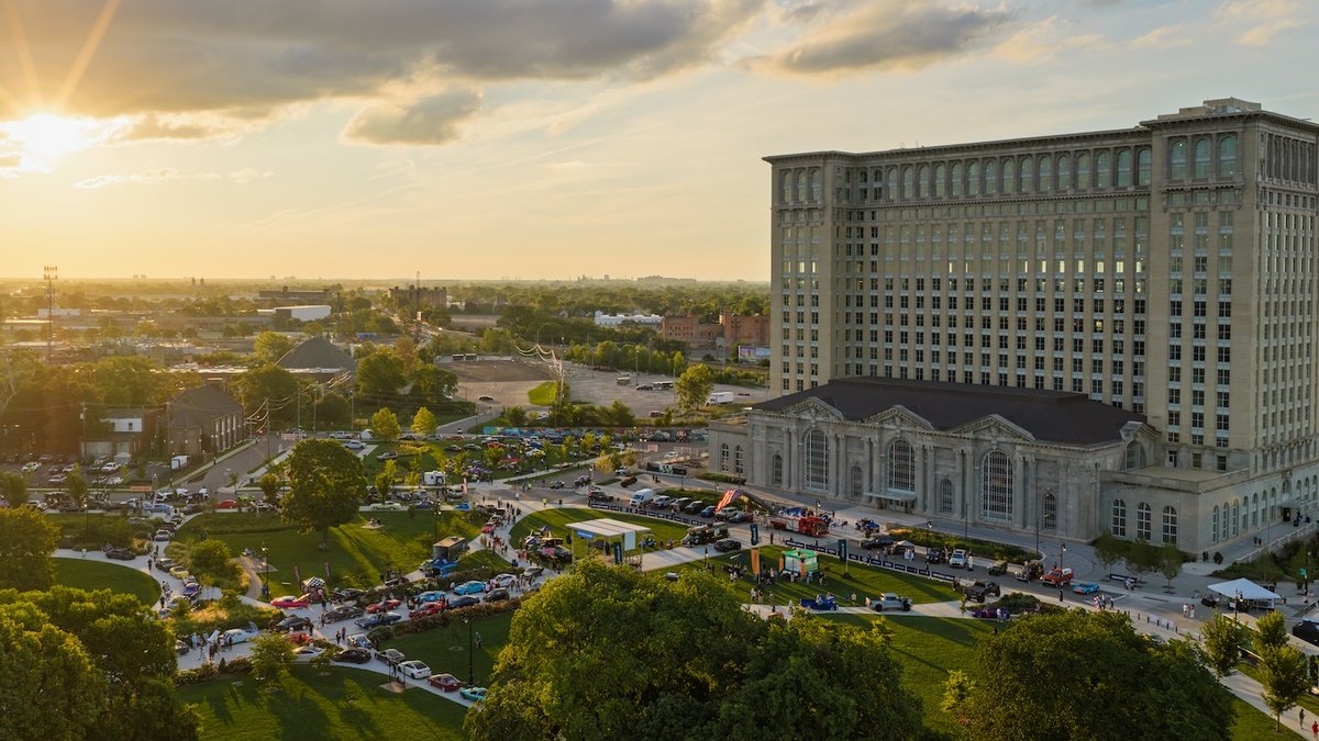 Detroit transforms abandoned sites into cultural landmarks Aerial view of a large, historic building beside a park with many people, tents, and cars gathered in the green space on a su