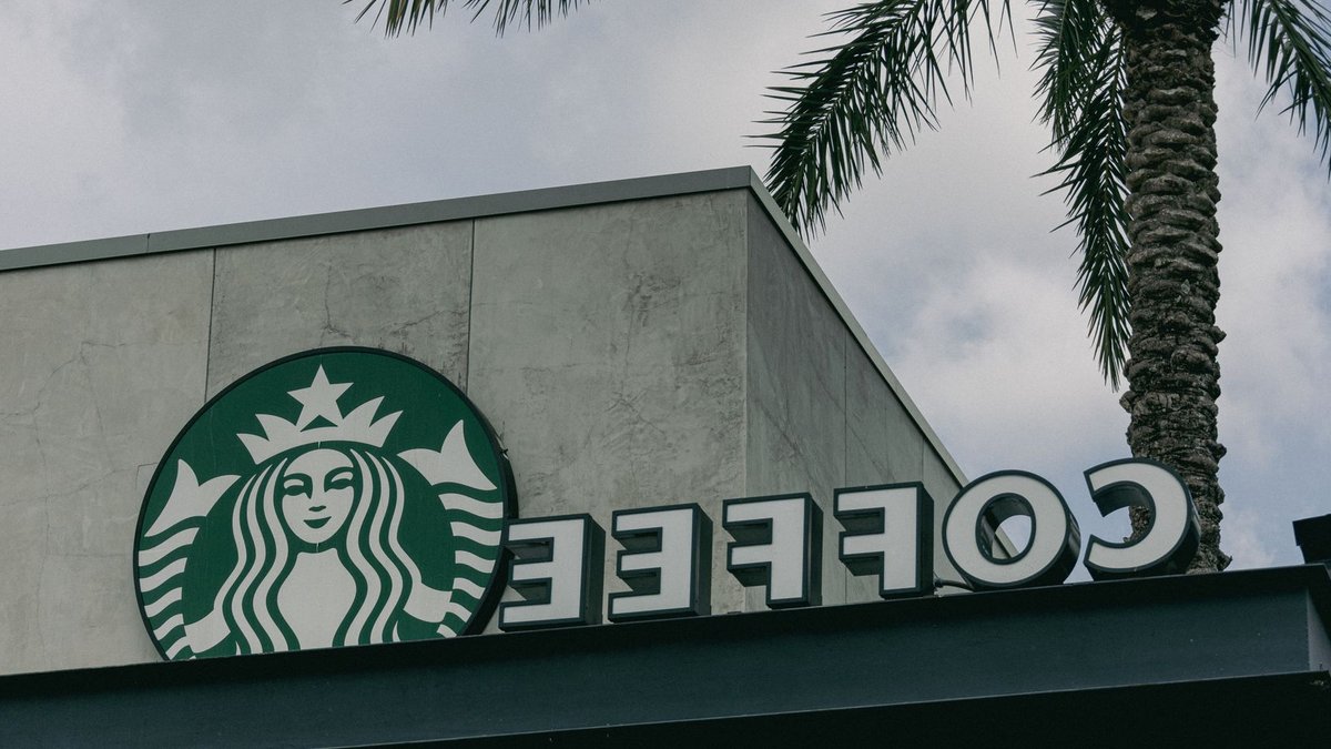 Low angle view of a Starbucks café sign with a palm tree against cloudy sky.