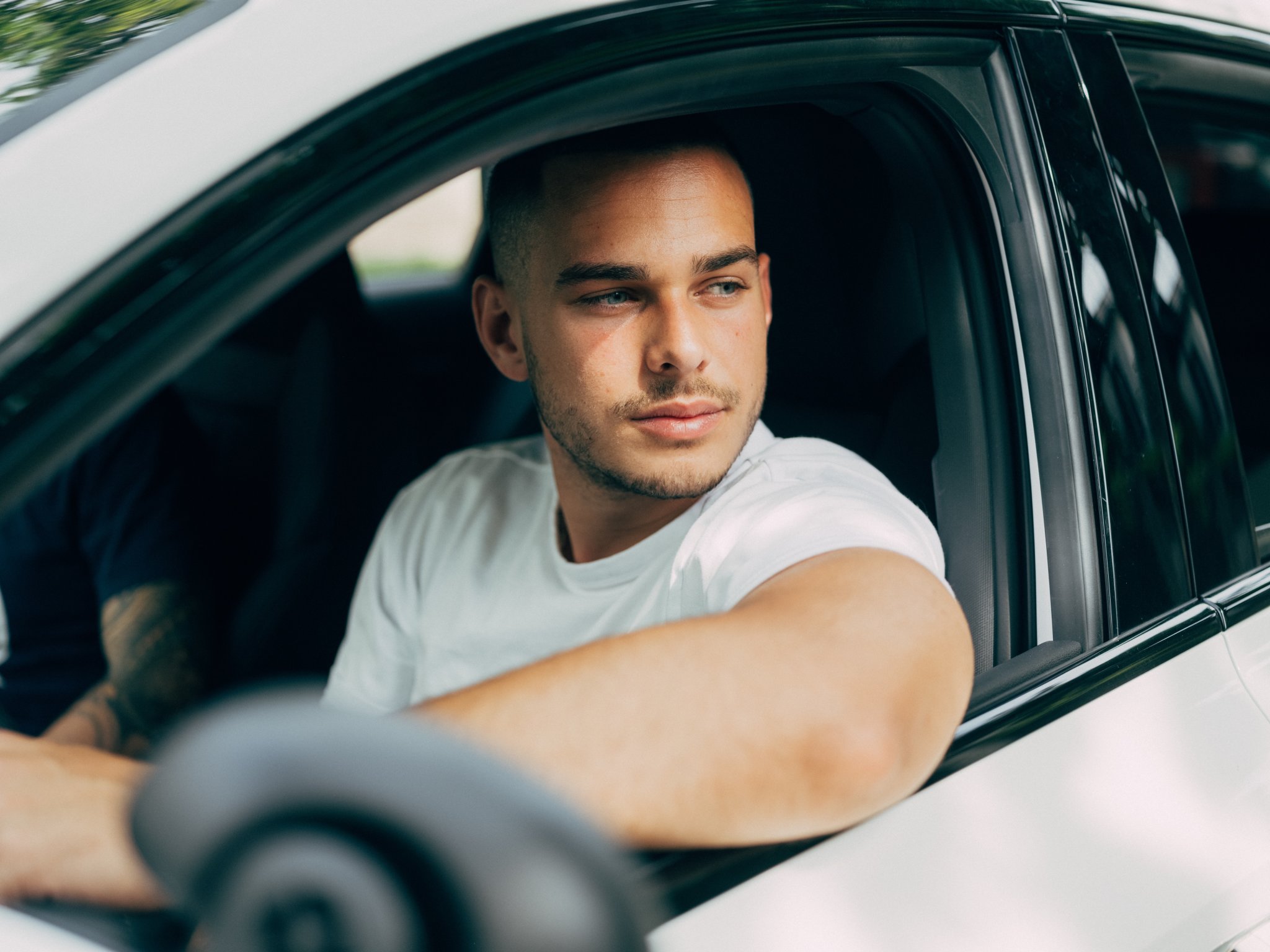 Junger Fahrschüler ist in Gedanken versunken und schaut aus dem weissen Fahrschulauto heraus