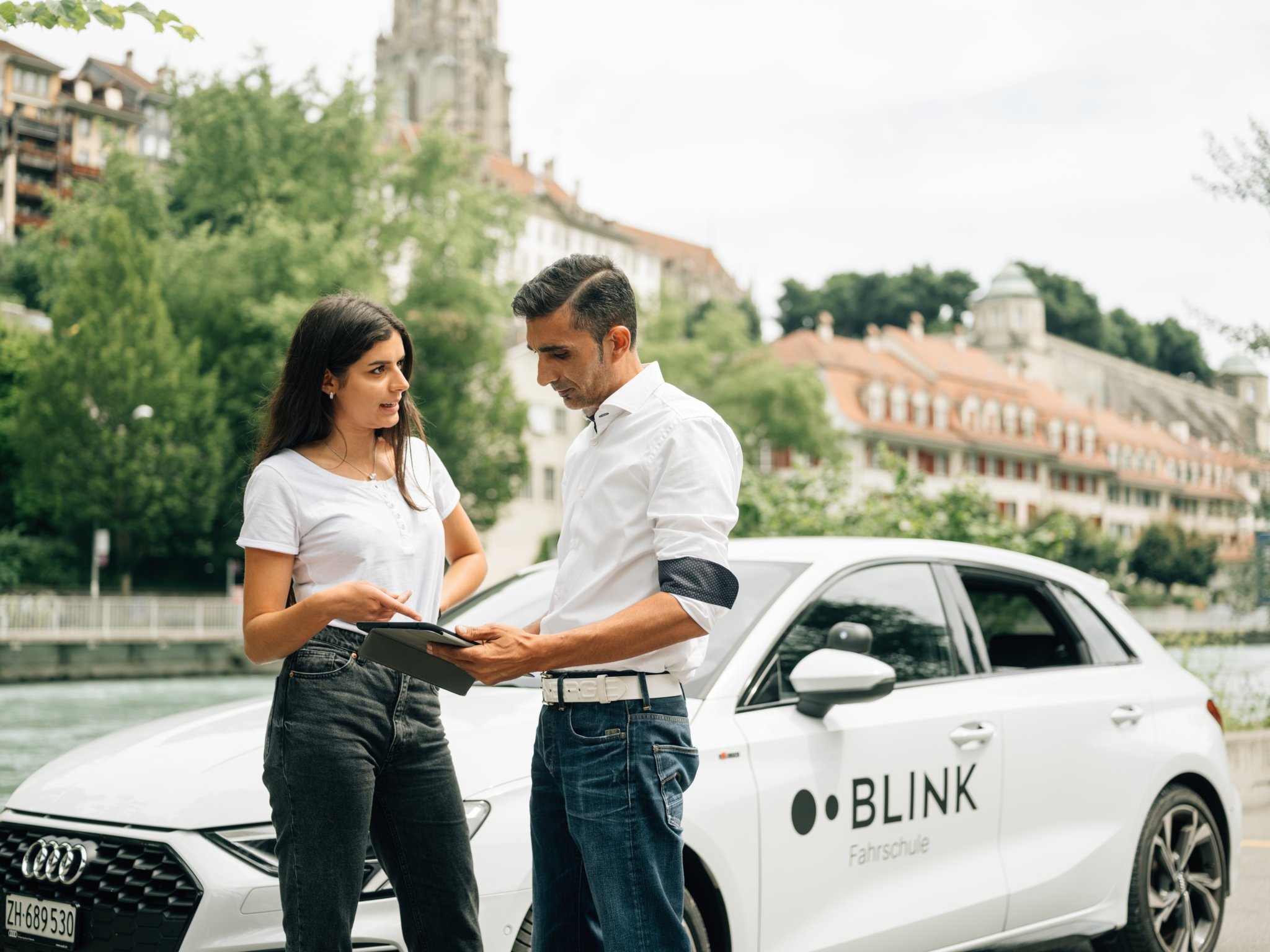 Eine Fahrschülerin bei BLINK in Oftringen steht vor dem Fahrschulauto und fragt ihren Fahrlehrer etwas mit einem ernsten Gesichtsausdruck