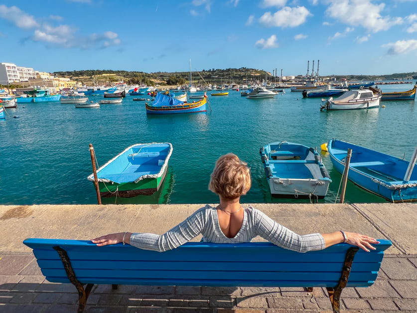 mulher sentada no banco observanda barcos em Malta