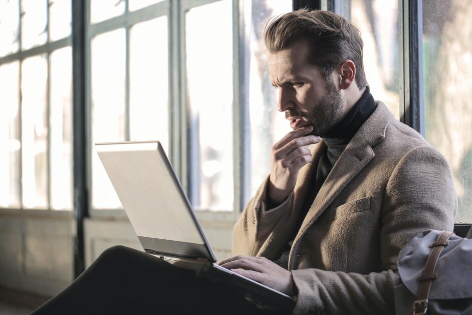 homem de terno sentado com notebook no colo 