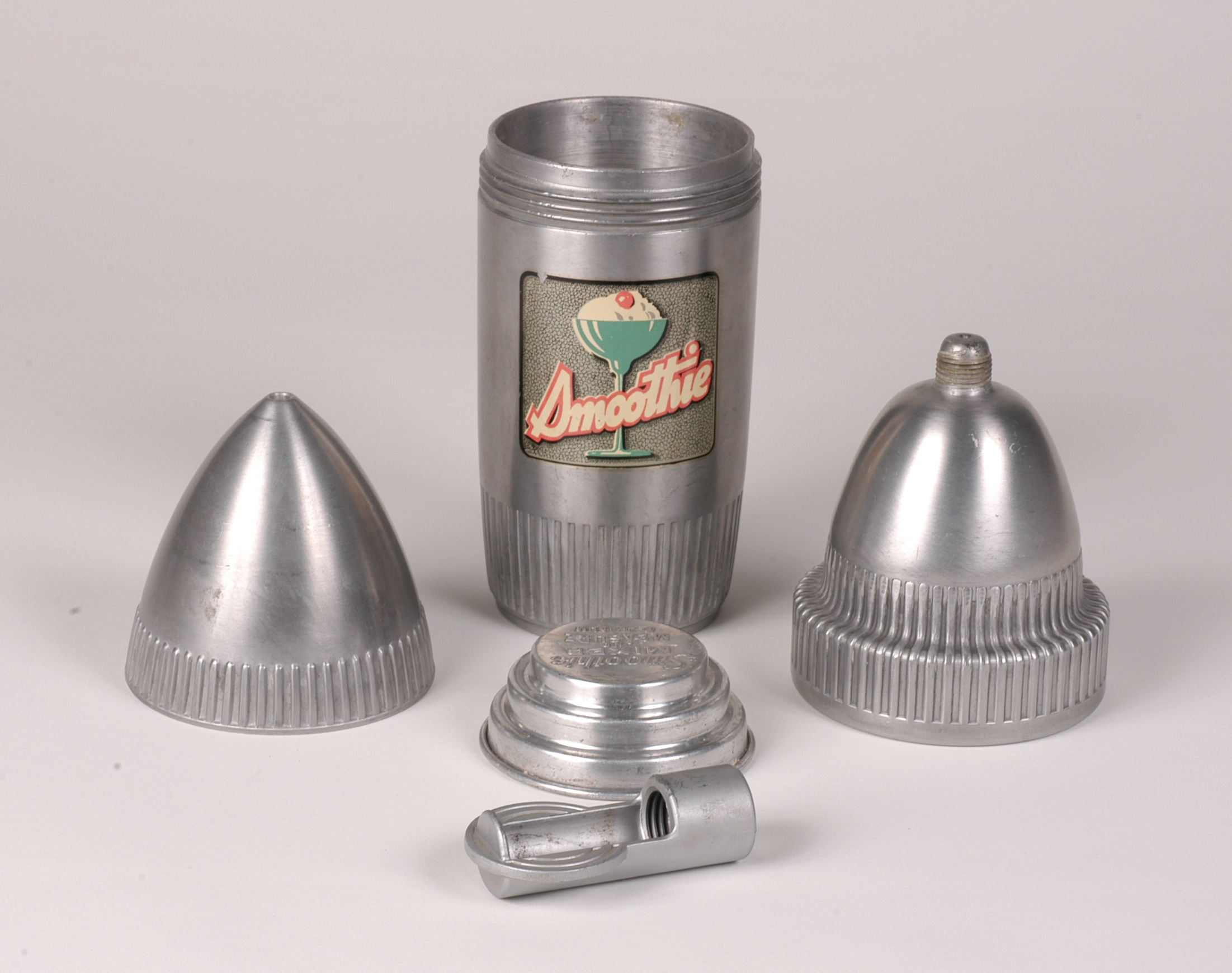 An aluminum hand mixer for making ice cream or whipped cream. It is made up of five parts, including a cylinder with two cone-shaped screw-on sections, which fit inside one another and attach to the main container.