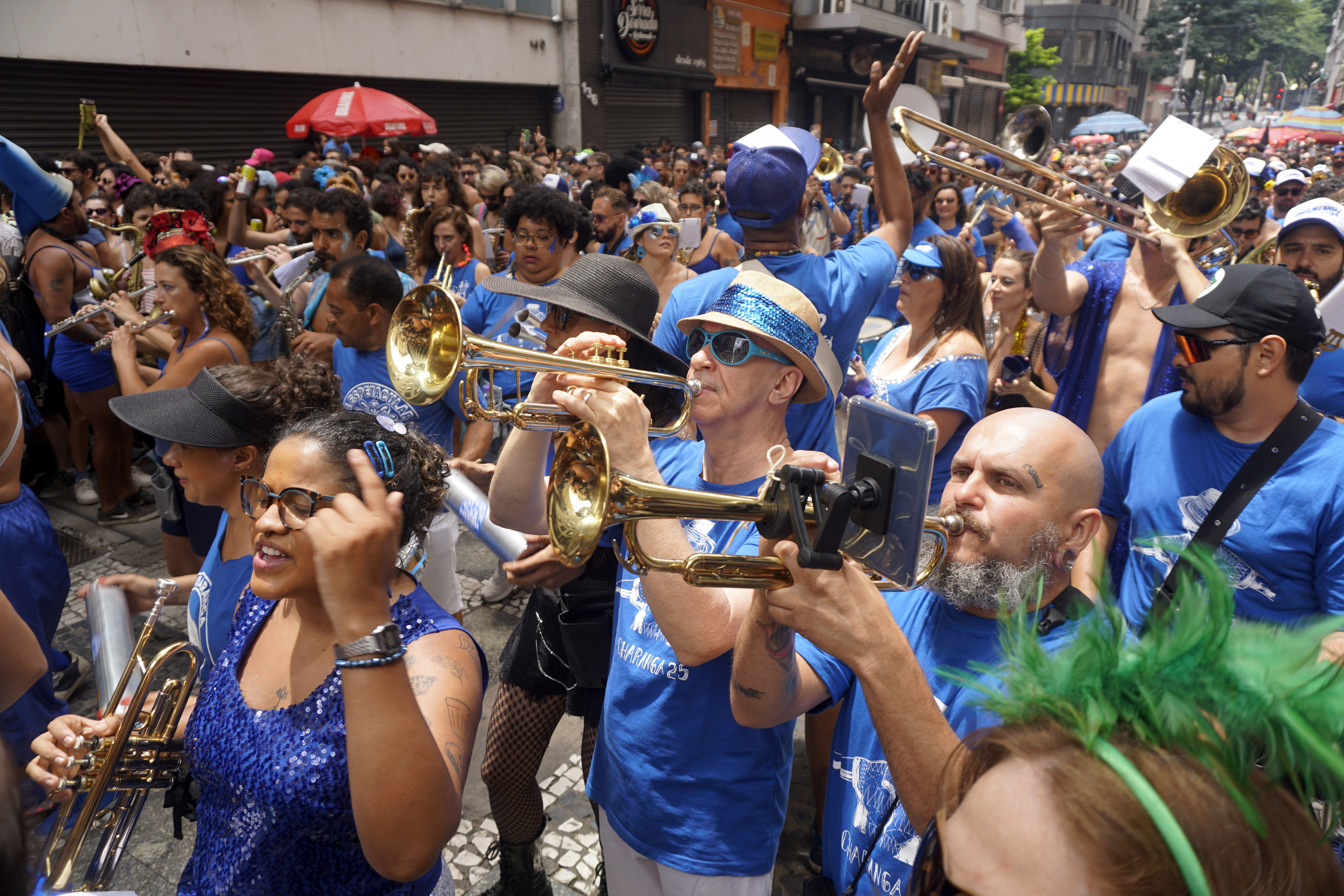 A photograph of musicians wearing matching blue t-shirts and playing a variety of musical instruments as they march in the Espetacular Charanga do Franca parade in Sao Paulo.