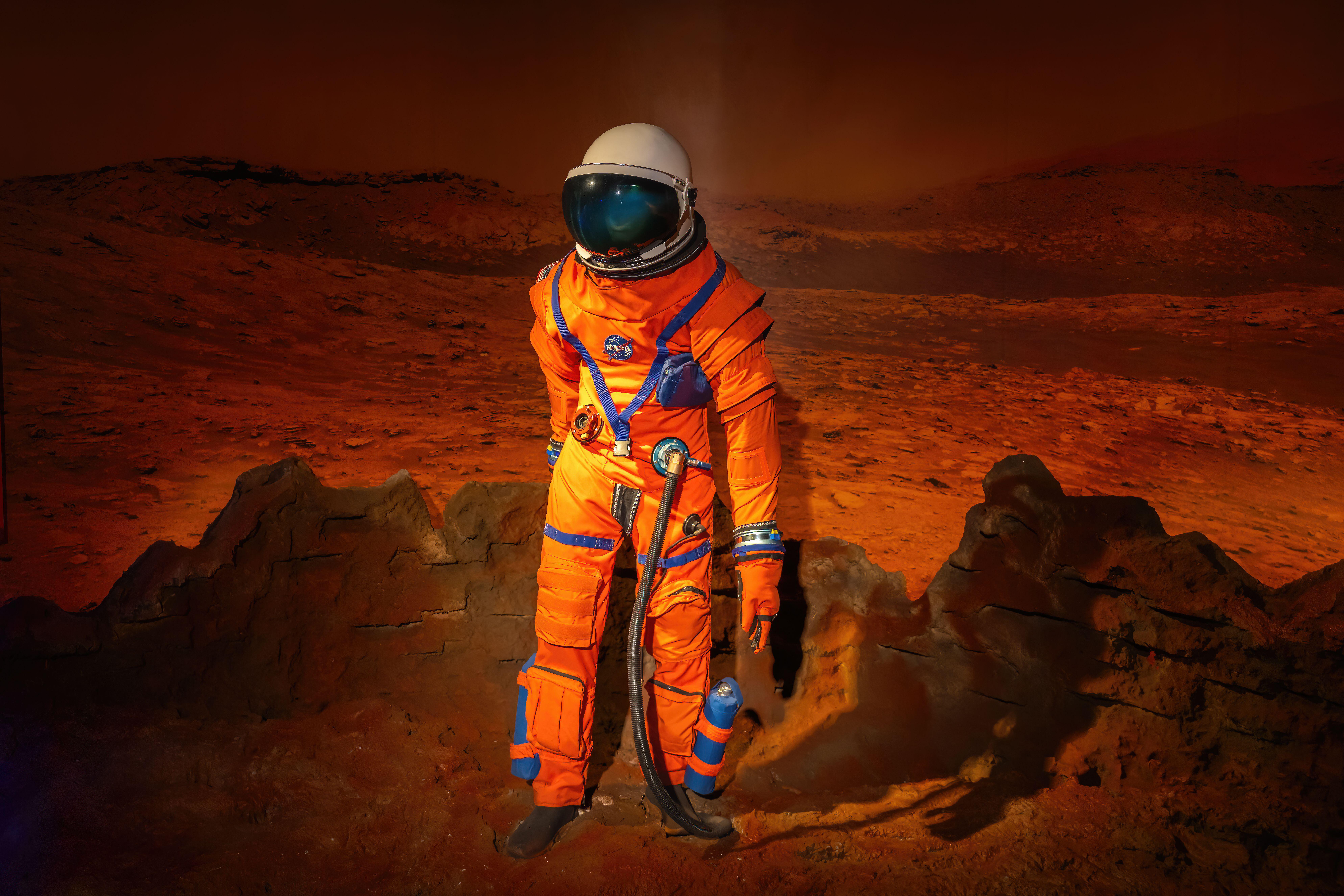 Astronaut in orange spacesuit standing on rocky Martian landscape