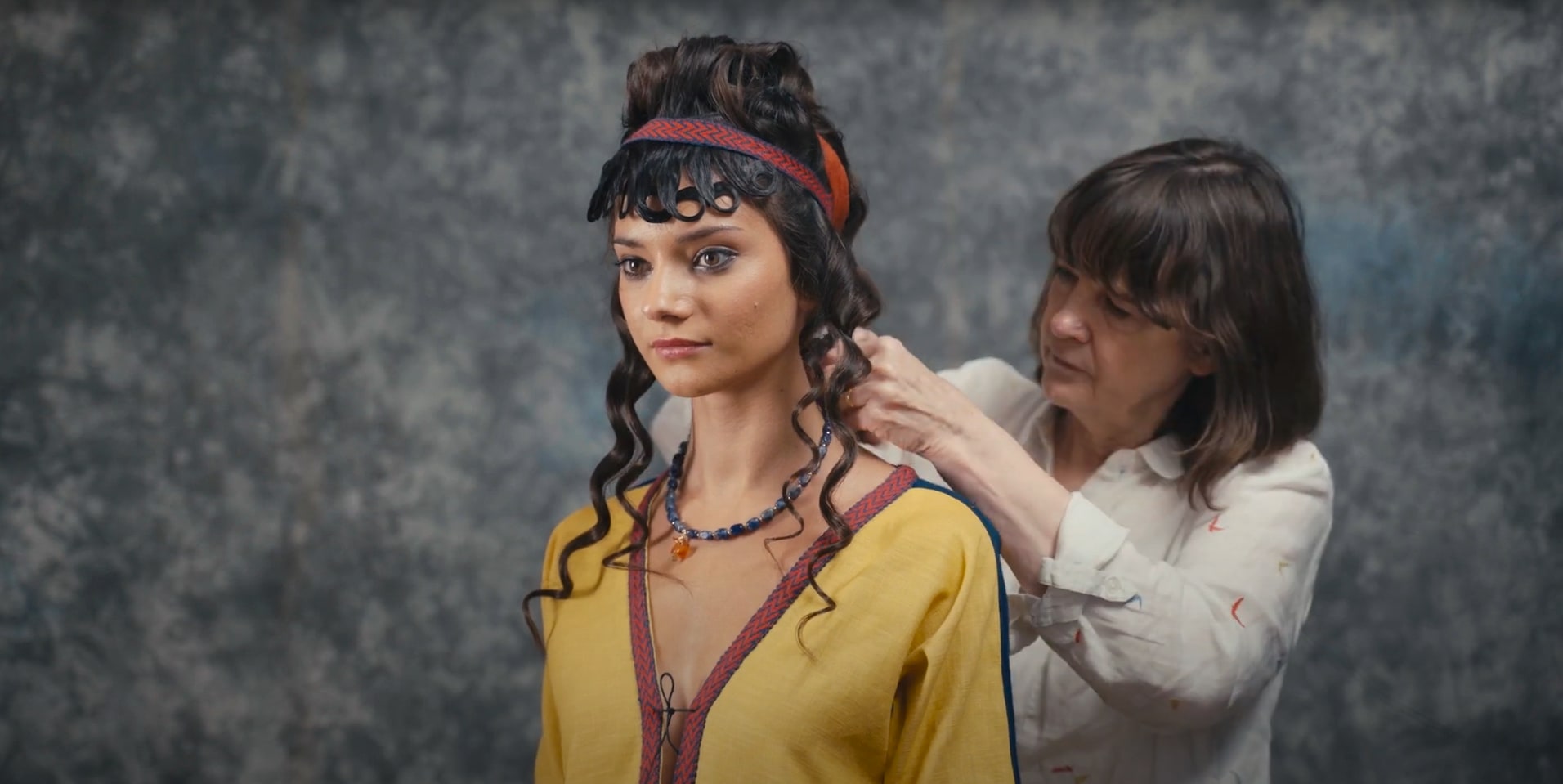 An image of Pauline Loven dressing a model in Mycenaean costume