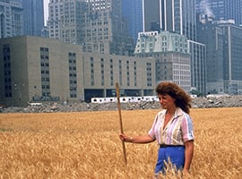 American environmental and conceptual artist Agnes Denes photographed standing in her installation, a two-acre wheat field with a city-scape in the background