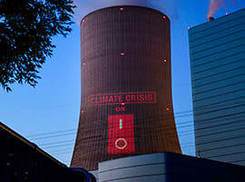 A slogan stating 'Climate Crisis On' projected onto a cooling tower of a coal-fired power plant