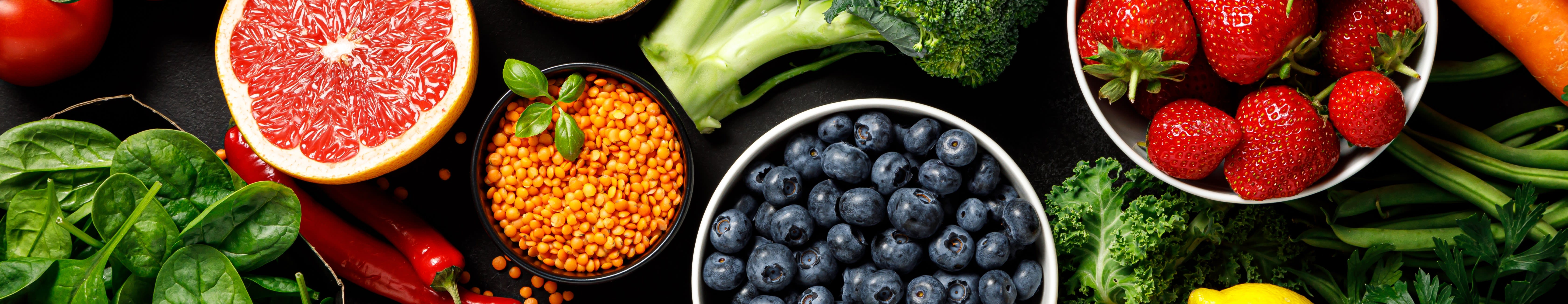 An overhead view of a selection of vegetables and fruits, artfully arrayed on a black tabletop