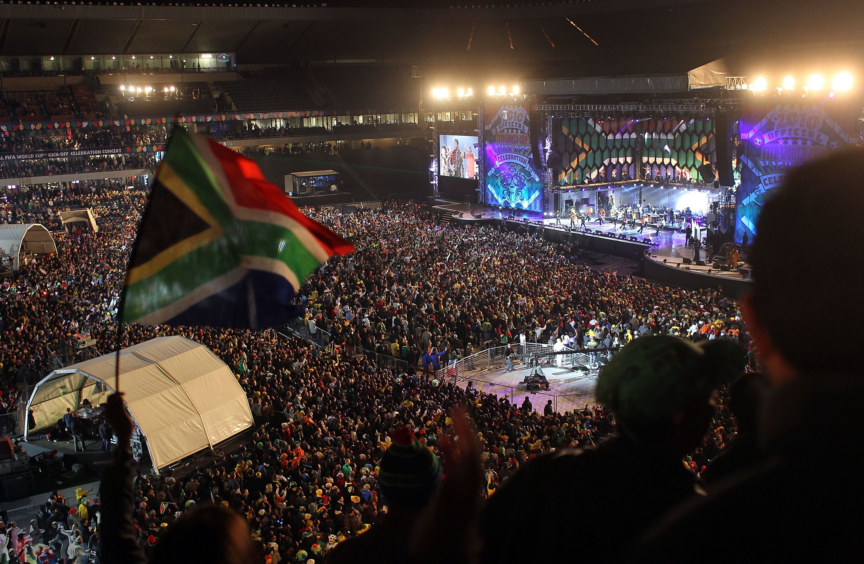 A photo of a large stadium-based concert, showing concert-goers wave the South African flag at the launch of the 2010 World Cup.