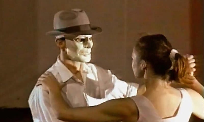 Two actors dancing with a man in a mask and the back of a woman's head