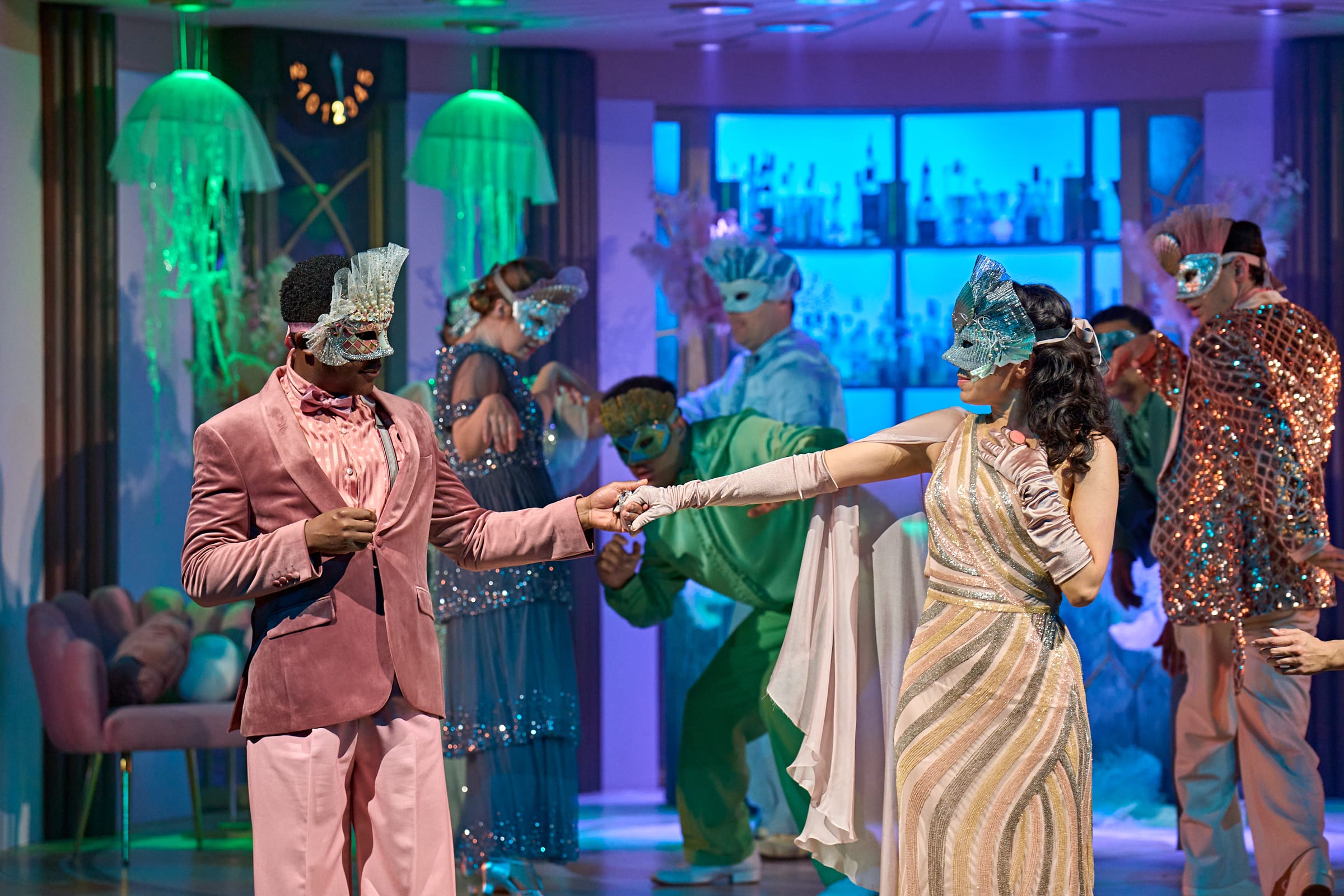 A group of actors on stage wearing masks and colourful costumes starring in Simon Godwin's production of Much Ado About Nothing.