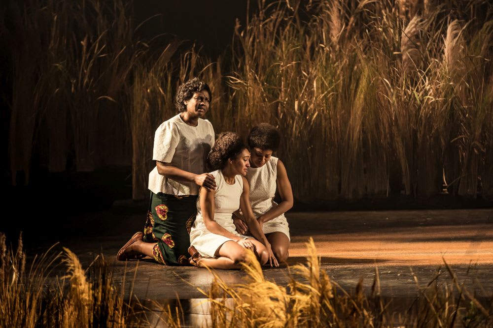 In Three Sisters, Sarah Niles, Natalie Simpson and Rachael Ofori kneel down and comfort one another against the backdrop of a grassland