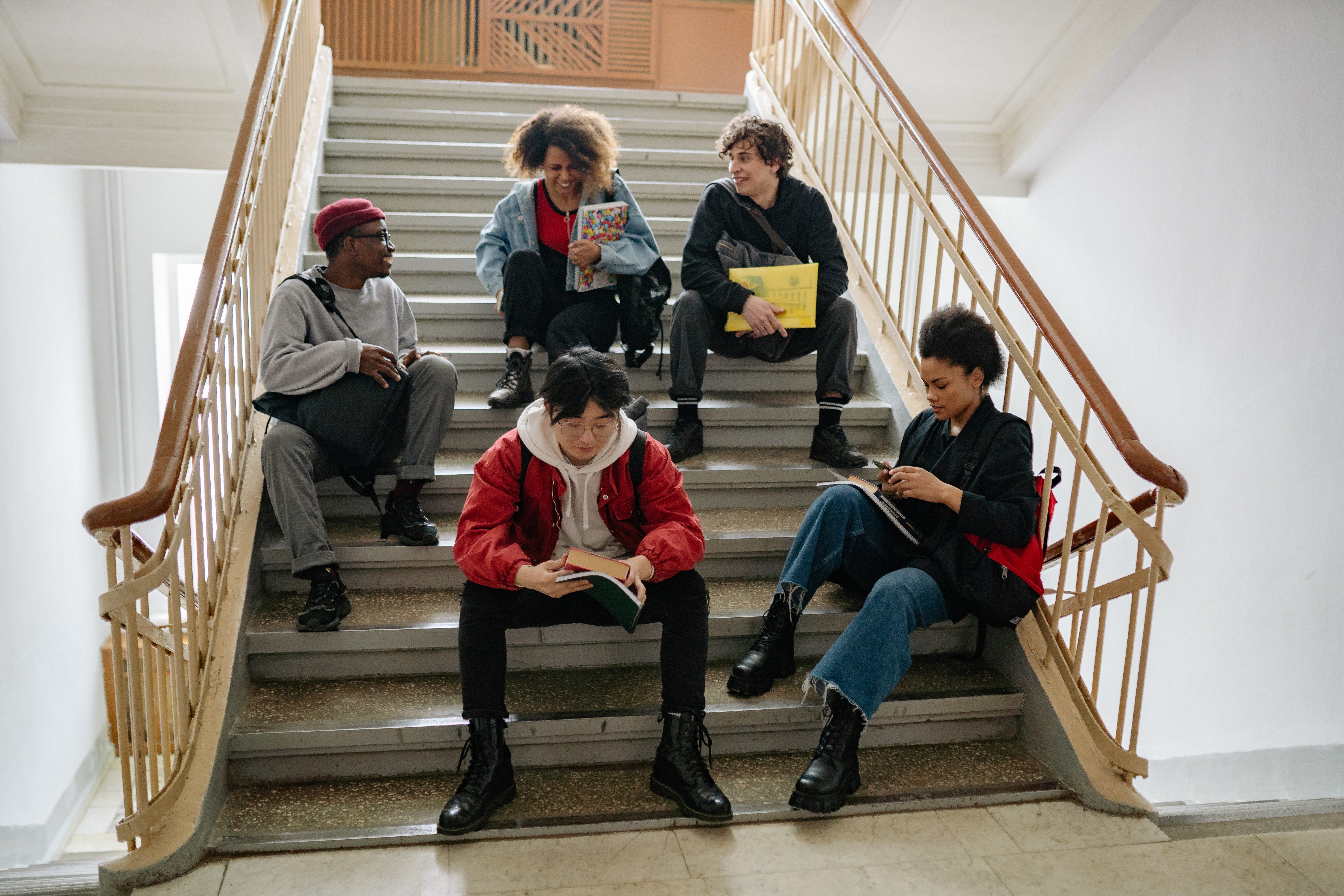 Secondary Education - Students sitting on an indoor staircase reading, talking, and using notebooks.