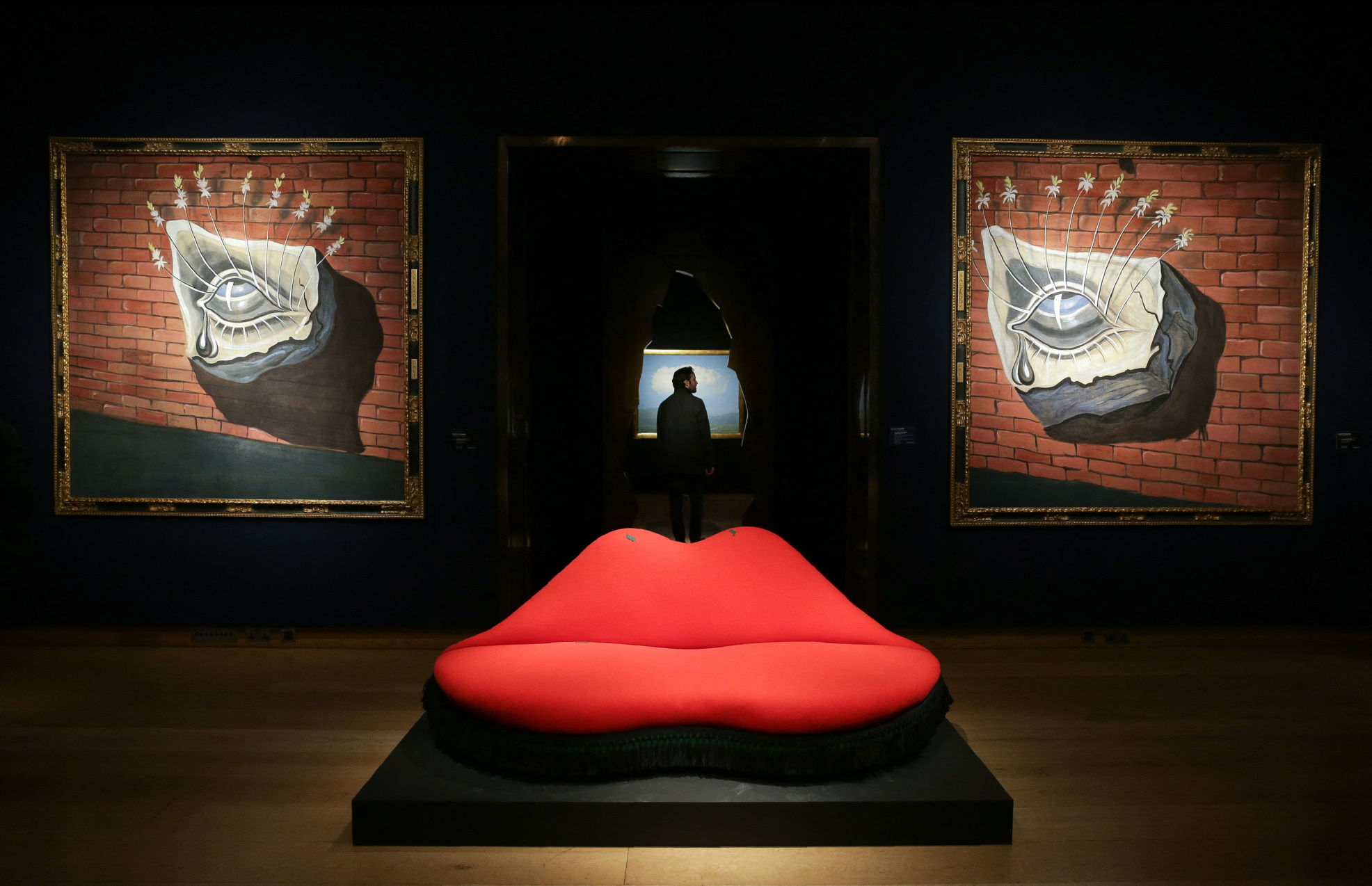 An artwork by Spanish artist Salvador Dali, entitled Mae West Lips Sofa, is pictured in front of artworks by Dali entitled L'oeil fleuri, décor pour le ballet Tristan fou during a photocall ahead of the Impressionist and Modern and Art of the Surreal sales at Christie's in London on February 24, 2017