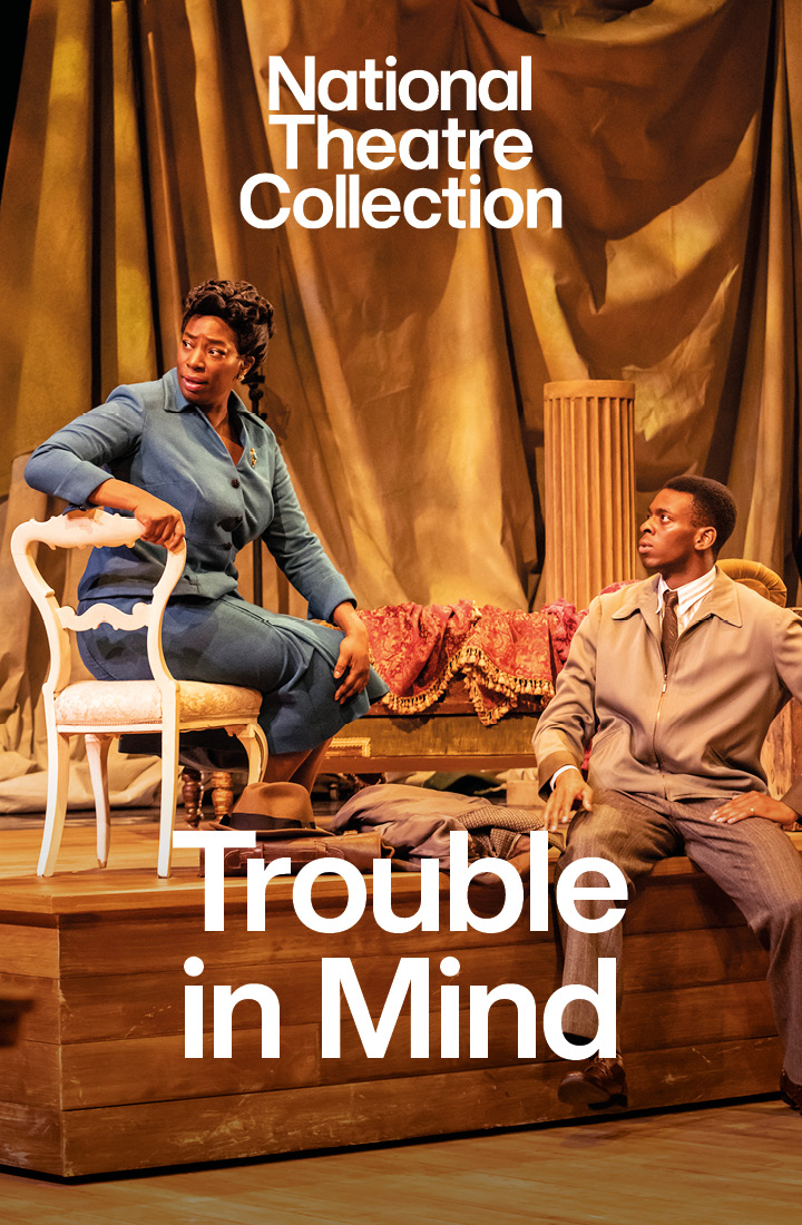 A man in a yellow waistcoat, white shirt and brown trousers has his hands against his torso whilst smiling open-mouthed