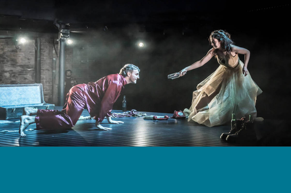 Picture of a scene of A Streetcar Named Desire featuring Paul Mescal on a bourdeaux suit extending his hand to an actress in a gold gown. Photo credit ©Marc Brenner