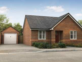 A brick bungalow with a detached garage sits on a paved driveway in front of a wooded area under a cloudy sky.