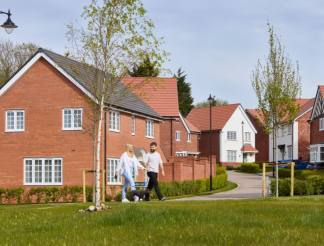 A residential neighborhood with brick houses, a grassy lawn, and a couple walking down the path.