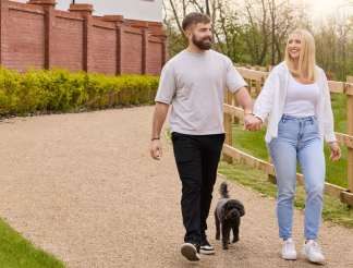 A young couple, a man with a beard and a woman, are walking together on a path surrounded by a brick wall and greenery.