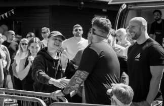 In the foreground, two men shake hands while a crowd watches in the background.