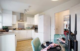 A modern, minimalist kitchen with white cabinets, stainless steel appliances, and a dining area with a patterned rug and chairs.