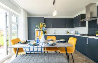 A modern kitchen with dark cabinets, a dining table with yellow chairs, and a vase of flowers on the counter, all set against a bright and airy backdrop.
