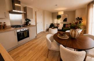 A modern kitchen with a dining table in the foreground transitions into a cozy living room with a sofa and artwork in the background.