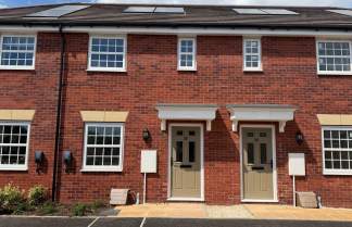 Two identical brick townhouses with tan doors and white-framed windows stand in the foreground, while a bright blue sky with scattered clouds forms the background.