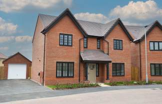 A modern brick house with a detached garage sits on a paved driveway under a cloudy sky.