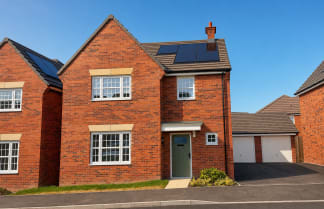 A row of modern brick houses with solar panels on their roofs are set against a clear blue sky.
