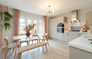 A modern dining area with a light wood table and bench is in the foreground, while a sleek kitchen with light gray cabinets and stainless steel appliances is in the background.