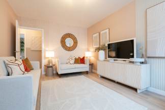 A light-colored sofa and rug fill the foreground of a living room with a television and artwork adorning the peach-colored walls in the background.