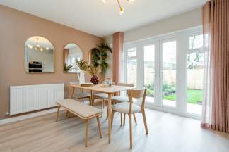 A light wood dining set with a bench and chairs sits on a light wood floor in the foreground, while a wall with arched mirrors and a radiator is on the left, and large glass doors opening to a green backyard are on the right.