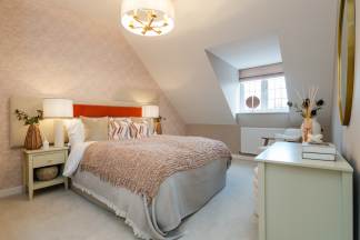 A cozy bedroom with a plush bed in the foreground and a sloped ceiling with a window in the background.
