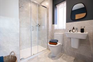 A modern bathroom with a glass shower enclosure, a white sink, and a black framed mirror on the wall.