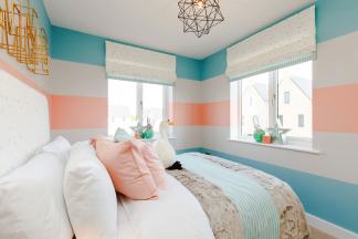 A cozy bedroom with a plush bed in the foreground and a view of houses through the windows in the background.