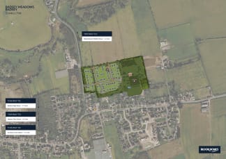 The image appears to be an aerial view of a residential development, with a grid-like layout of houses and streets in the foreground, surrounded by open fields and rural areas in the background.