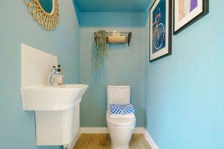 A cozy and vibrant bathroom with a white pedestal sink, a toilet, and a wall adorned with a wire basket, a framed artwork, and a decorative wall hanging against a soothing turquoise blue backdrop.
