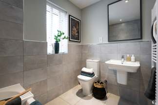 A modern and minimalist bathroom with gray tile walls, a pedestal sink, and a framed artwork on the wall, along with a potted plant and towels neatly arranged.