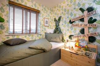 A cozy and vibrant bedroom with a patterned wallpaper, a wooden bed frame, and various decorative elements such as a plush pillow, a lamp, and a sign with a dinosaur-themed message.