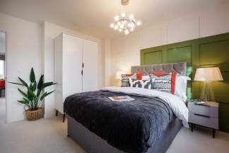 A cozy and stylish bedroom with a large bed, a green built-in wardrobe, and a chandelier hanging from the ceiling. A potted plant adds a touch of greenery to the space.
