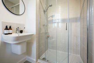 A modern, minimalist bathroom with a white sink, a round mirror, and a glass-enclosed shower area.